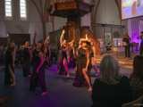 Dansgroep op podium met microfoon in Nicolaikerk bij aftrap 80 jaar vrijheid. Alle dansers doen dezelfde pose.