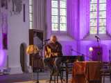Man speelt gitaar op podium in Nicolaikerk bij aftrap 80 jaar vrijheid.