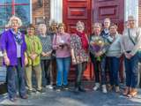 Grote groepsfoto voor gebouw, mensen houden Pelikaan-prijs en bos bloemen vast.