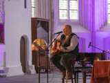 Man speelt gitaar op podium in Nicolaikerk bij aftrap 80 jaar vrijheid.