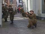 Verklede soldaat zit op grond met geweer bij Living History Appingedam. In de achtergrond staan meer verklede soldaten toe te kijken.